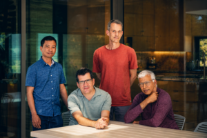 Jeff Dean in a cinematic high-definition portrait standing with fellow technology leaders in a modern office, featuring professional lighting and an editorial-style finish.