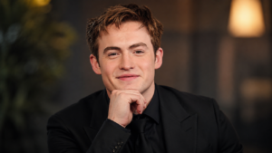 Kit Connor wearing a black suit in a cinematic portrait with warm lighting and a blurred luxury background, showcasing the British actor known for his rising Hollywood career.