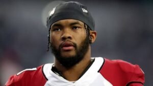 Kyler Murray wearing a red-and-white football uniform and black head covering during a game.
